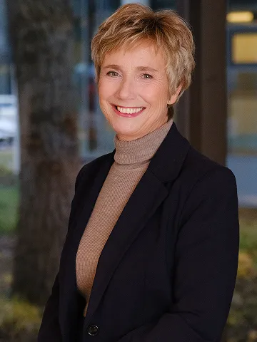 Amelie Fried lächelt in die Kamera, trägt einen dunklen Blazer und beigen Rollkragenpullover.